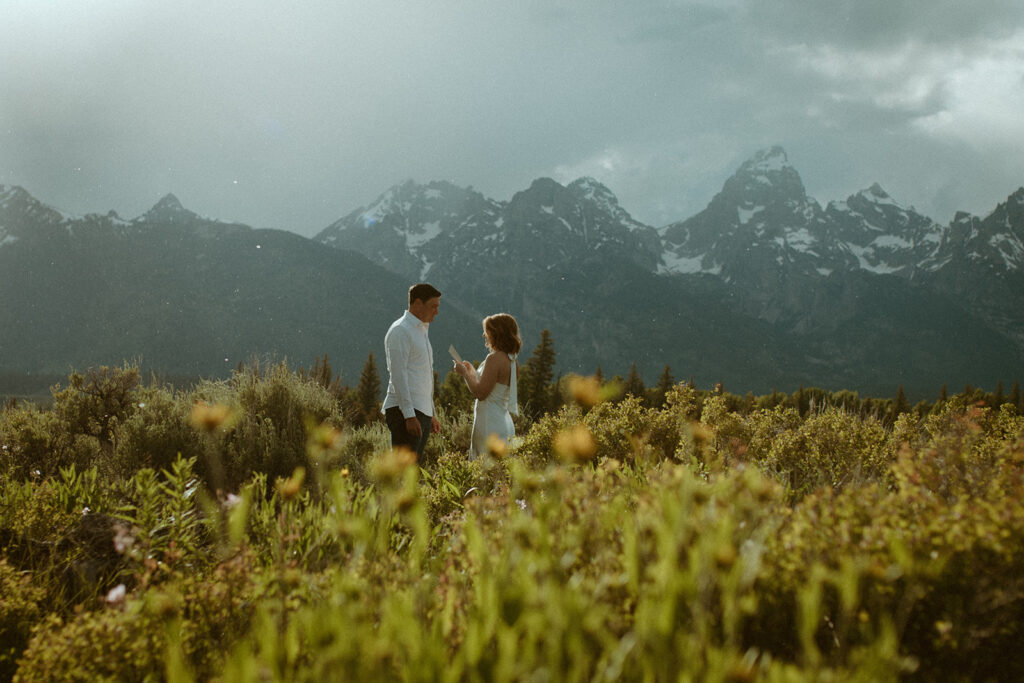 The most gorgeous rain filled golden back drop in Jackson Hole while they say their vows are you kidding me? Carlin + Andrews Grand Teton Elopement in the wildflowers.