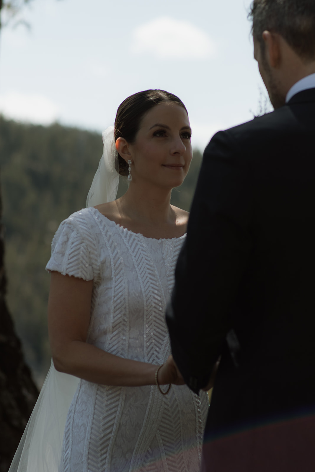 A wedding ceremony taking place outdoors, with a bride and groom standing in front of a large tree as an officiant reads from a book at the wedding tree in Jackson Hole