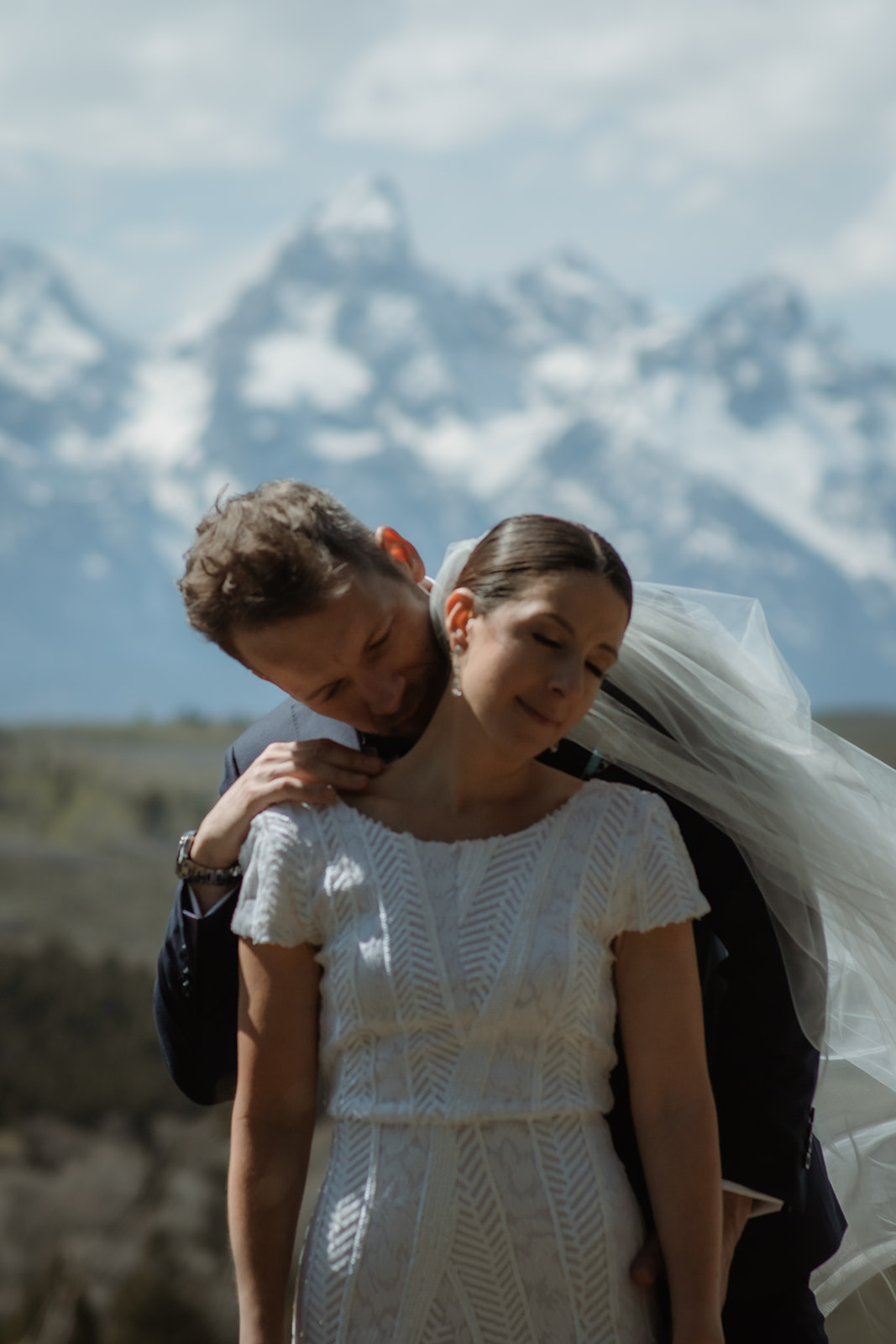 A bride and groom gaze at each other while standing outdoors with snow-capped mountains in the background. The bride holds a bouquet of flowers at the wedding tree in jackson hole