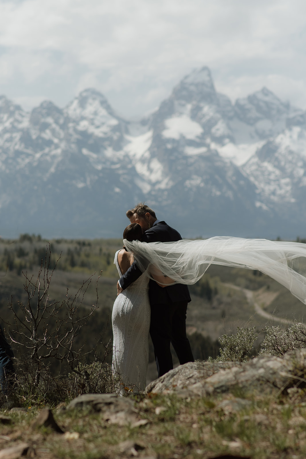 A bride and groom gaze at each other while standing outdoors with snow-capped mountains in the background. The bride holds a bouquet of flowers at the wedding tree in jackson hole