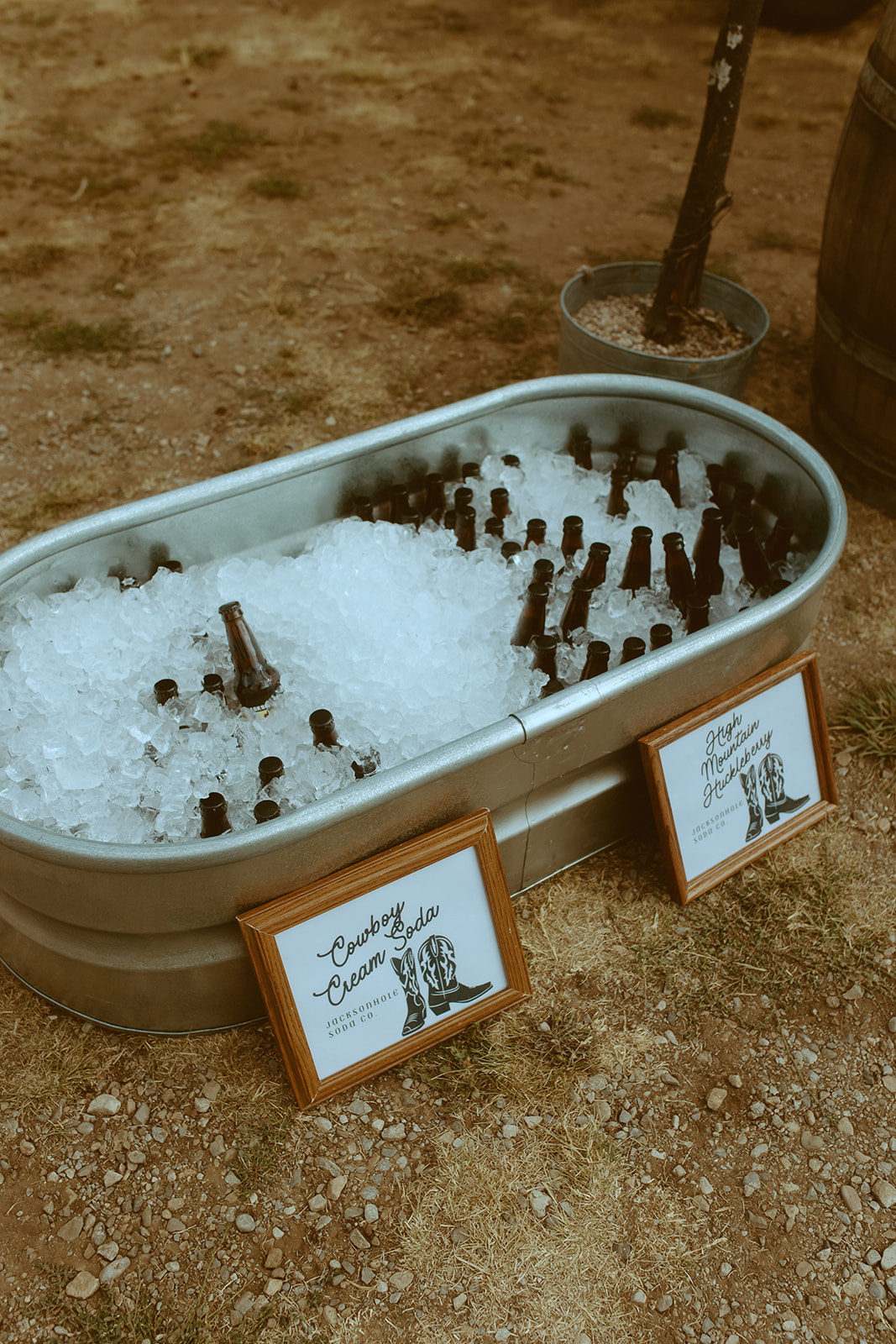 A metal basin filled with ice and bottled drinks at an outdoor event. A sign next to the basin reads "Cold Drinks.