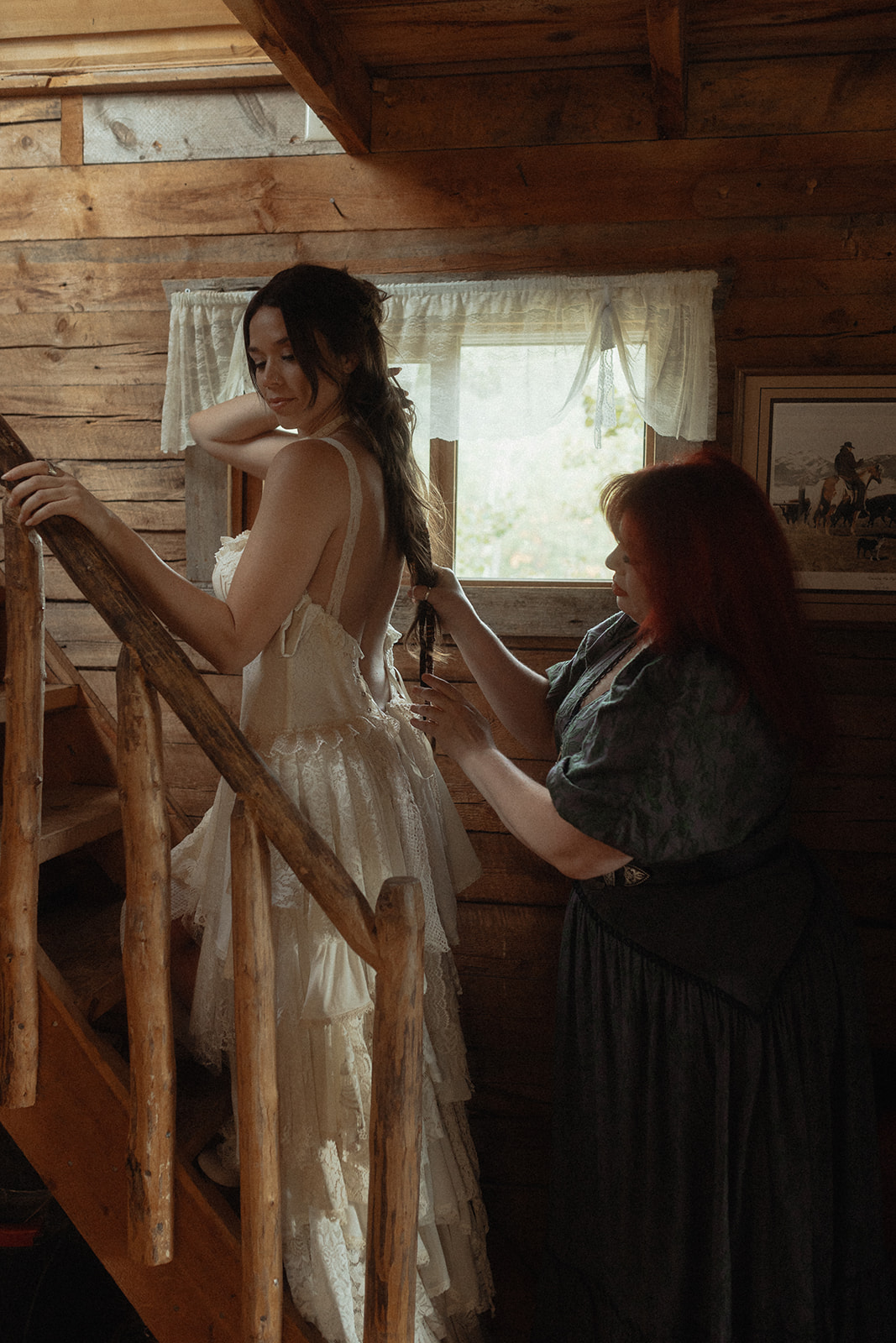 A woman in a white lace dress holds an intricate lace fan while standing in a rustic wooden room.