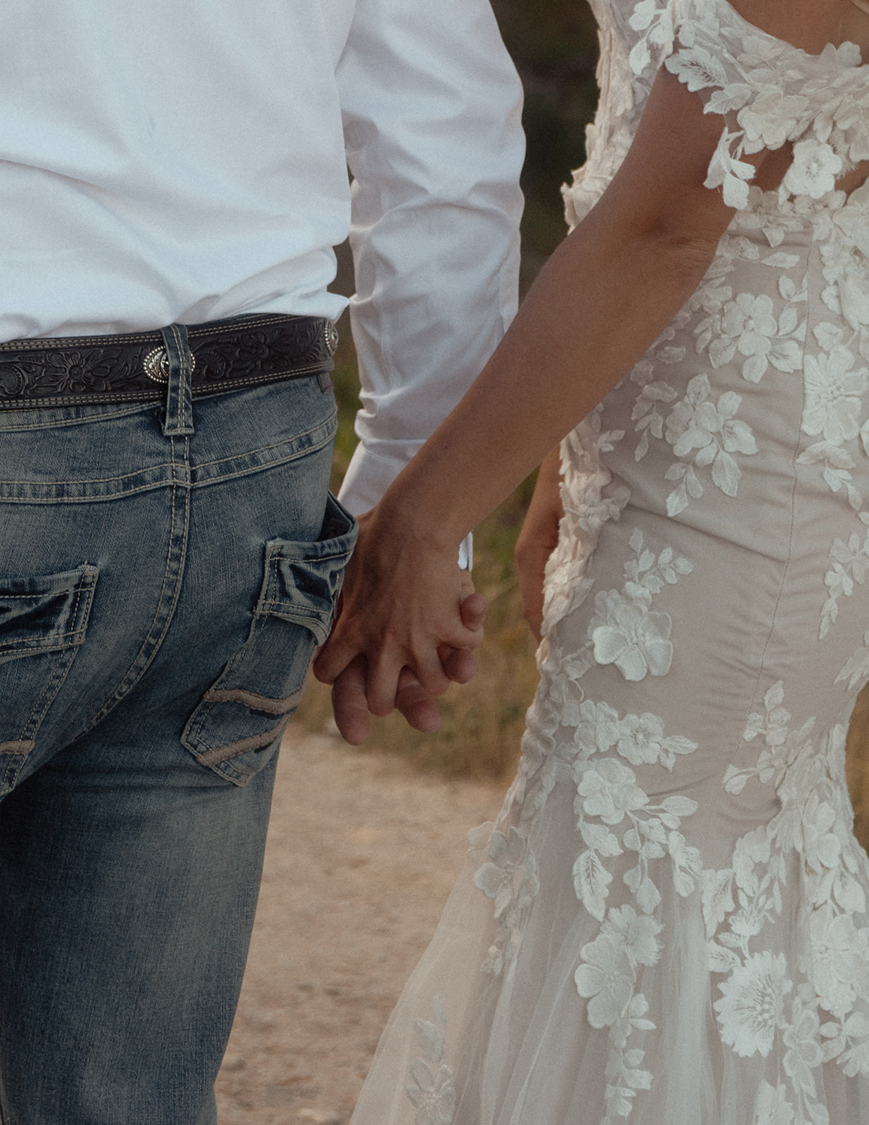 A person in a white shirt and blue jeans holding hands with another person wearing a white lace wedding dress.