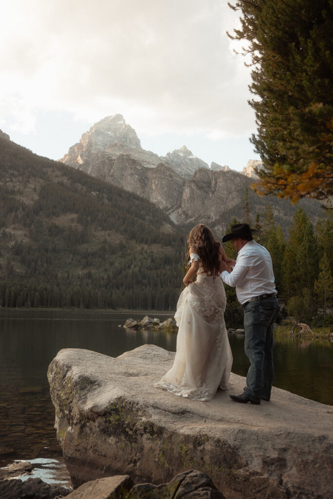 A man and woman in wedding dress standing on a rock by a lake for a Grand Teton National park taggart lake elopement