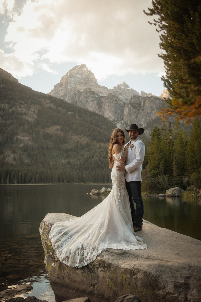 A man and woman in wedding dress standing on a rock by a lake for a taggart lake elopement