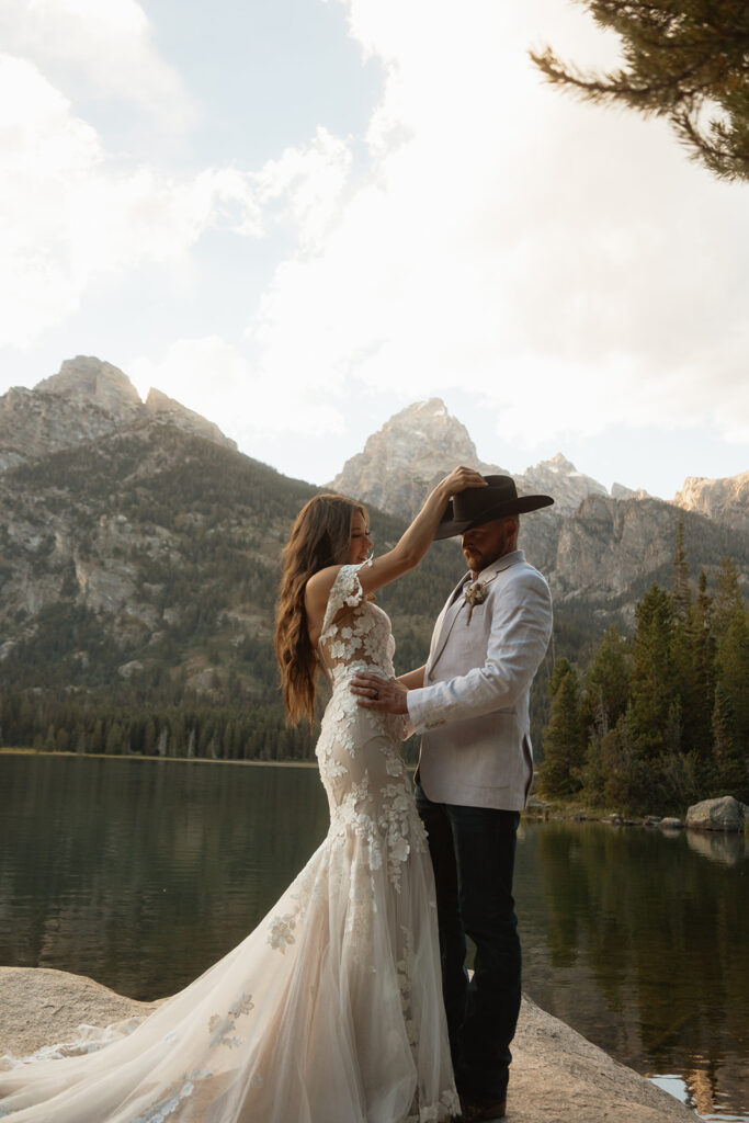 A man and woman in wedding dress standing on a rock by a lake for a taggart lake elopement