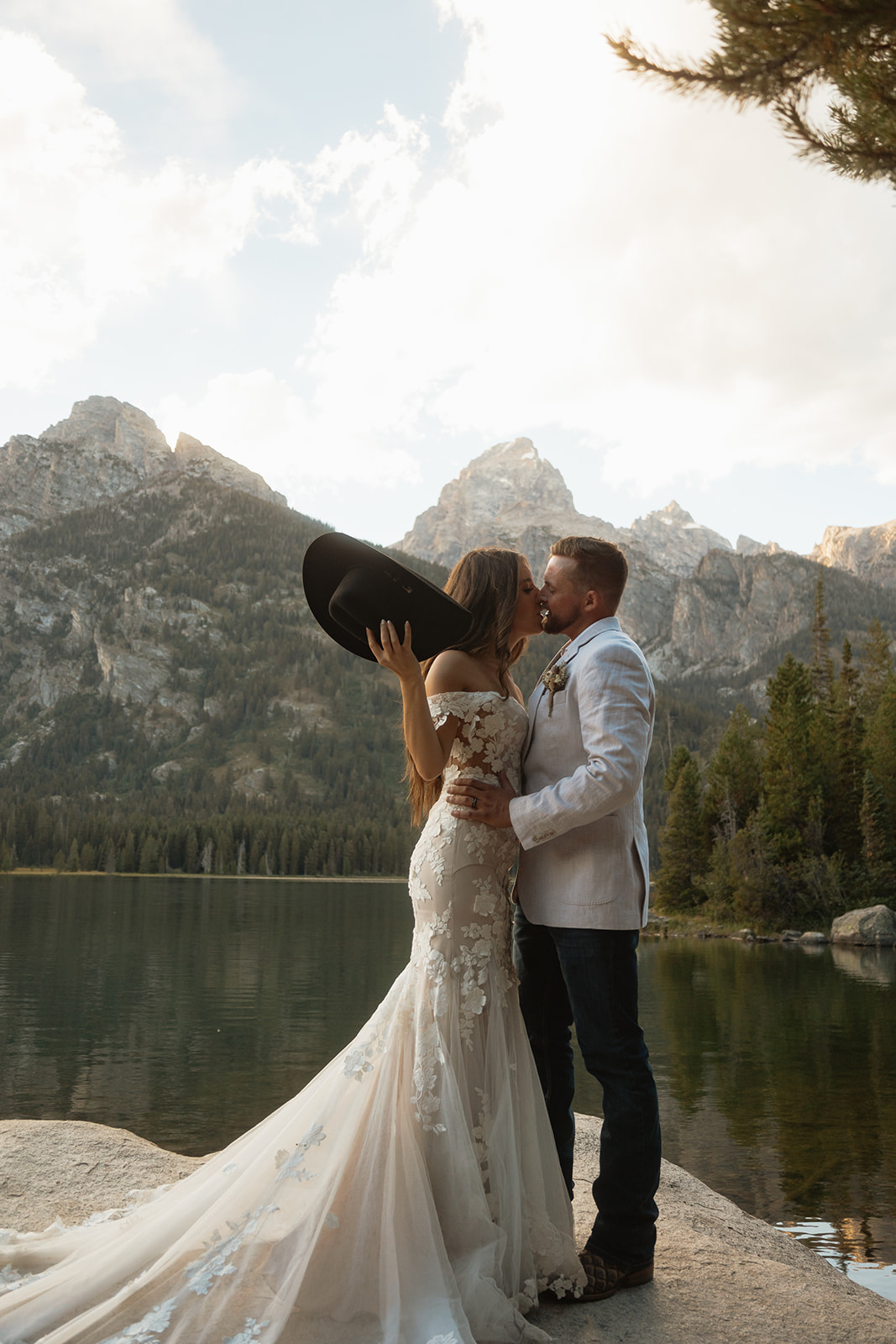 A man and woman in wedding dress standing on a rock by a lake for a Grand Teton National park taggart lake elopement