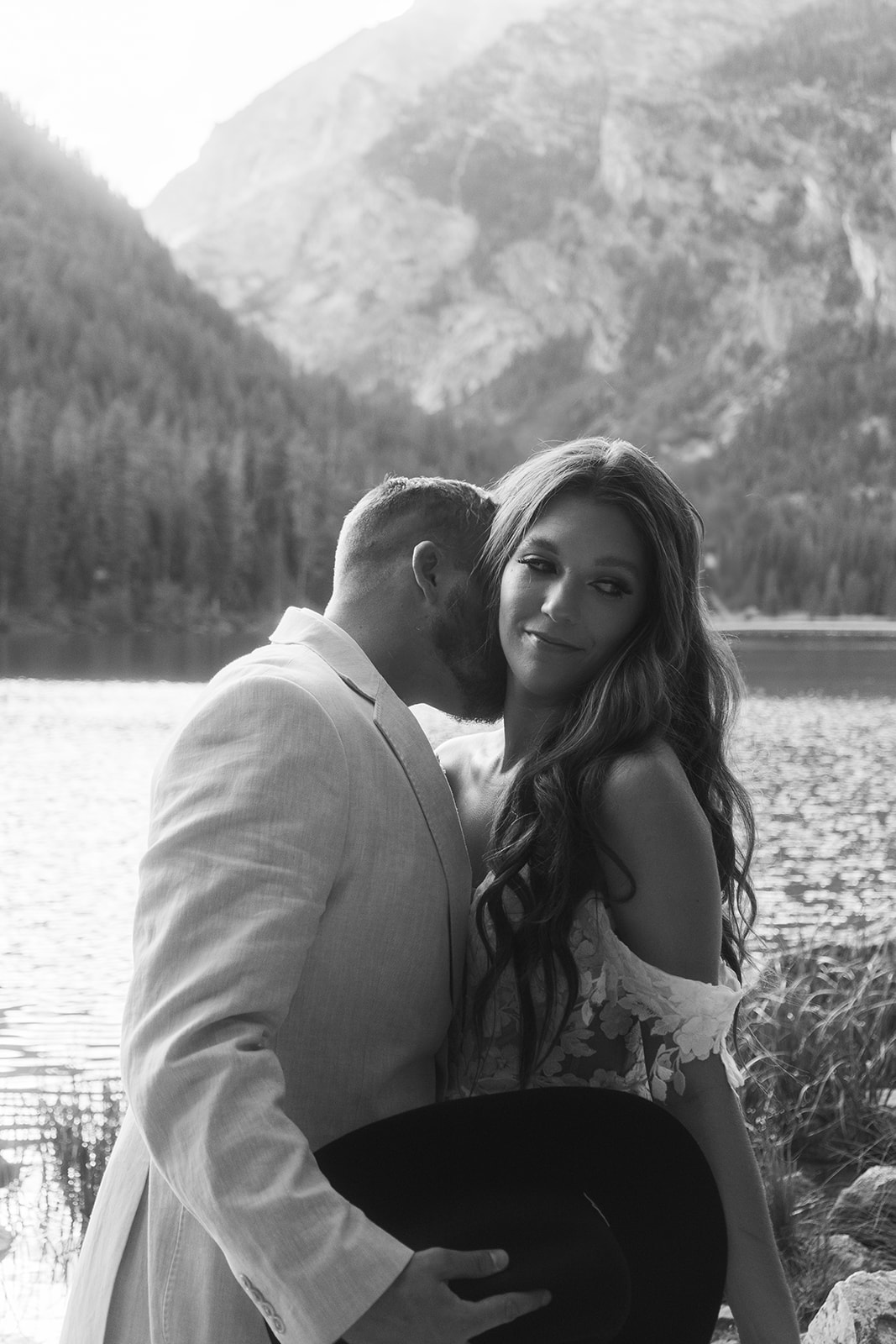 A man and woman in wedding dress standing on a rock by a lake for a Grand Teton National park taggart lake elopement