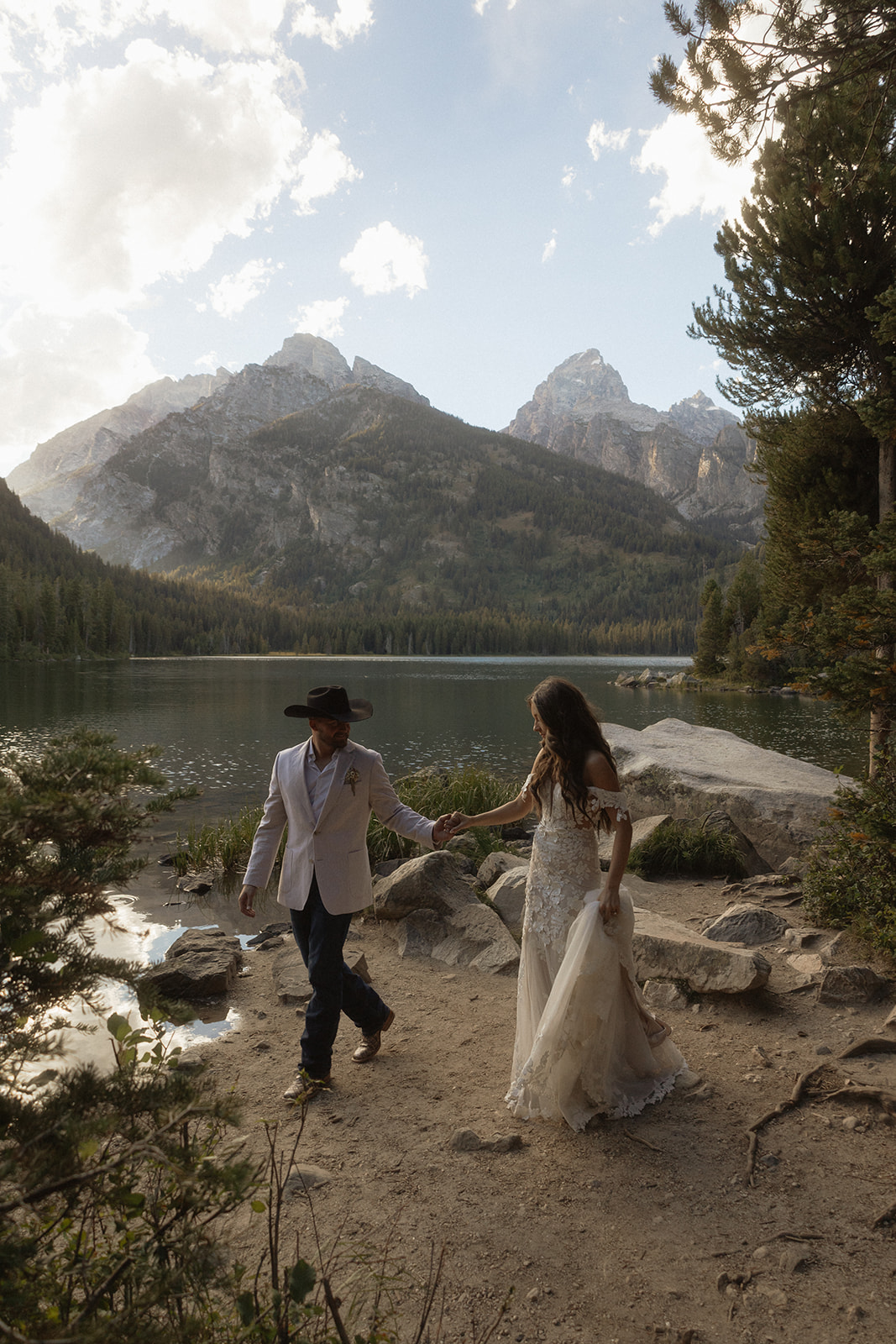 A man and woman in wedding dress standing on a rock by a lake for a Grand Teton National park taggart lake elopement