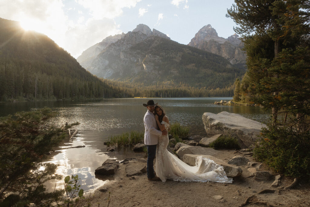 A man and woman in wedding dress standing on a rock by a lake for a Grand Teton National park taggart lake elopement