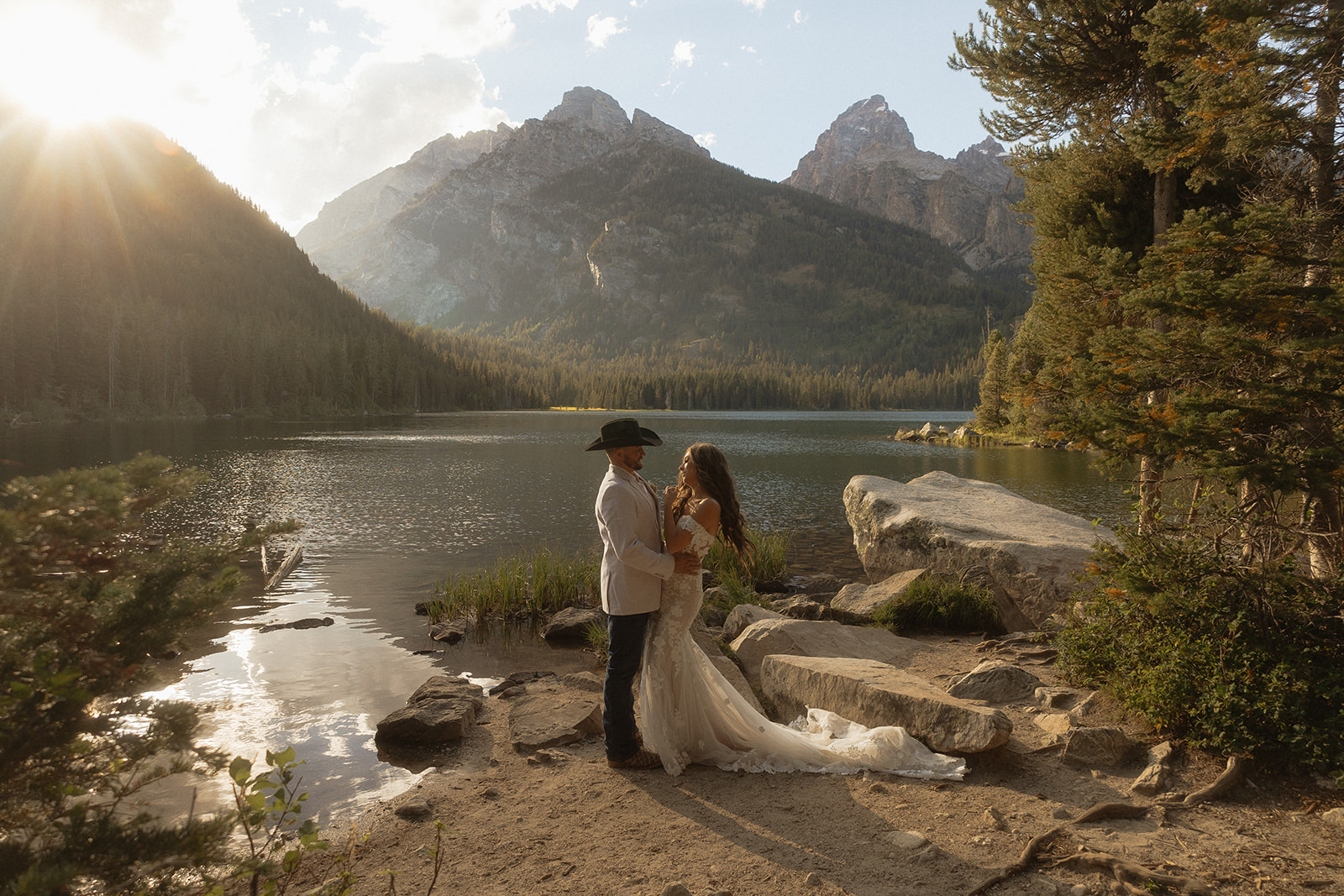 A man and woman in wedding dress standing on a rock by a lake for a Grand Teton National park taggart lake elopement