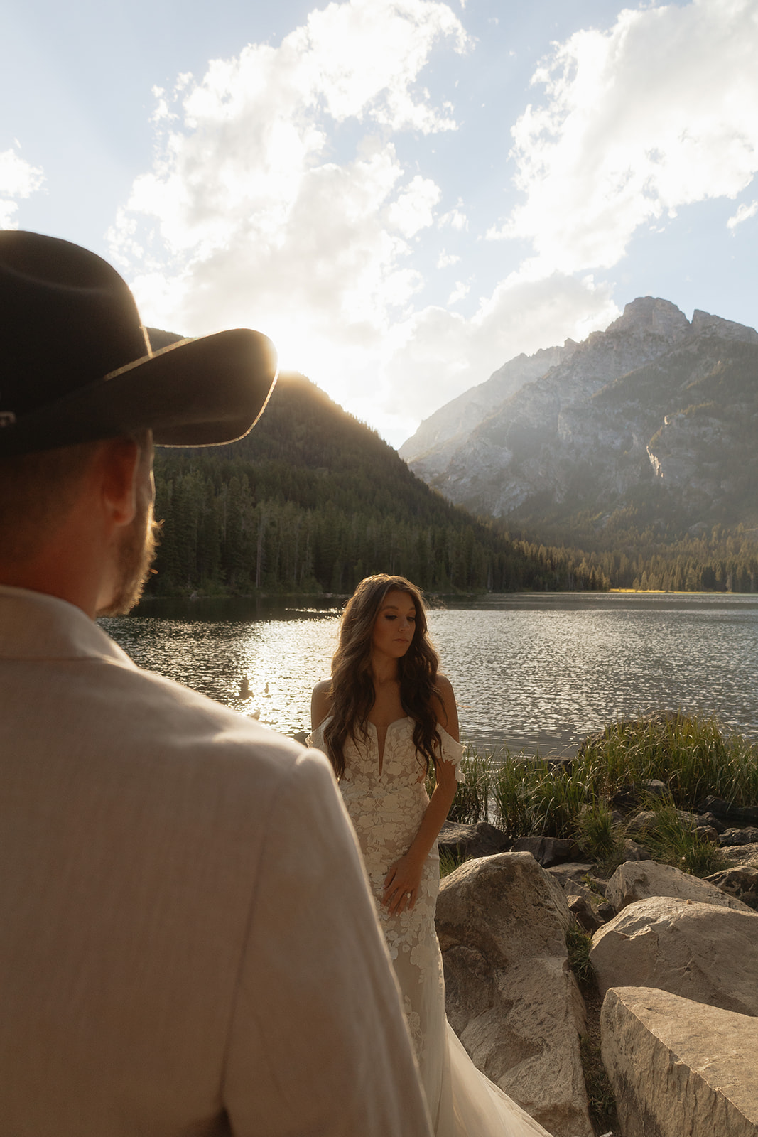 A man and woman in wedding dress standing on a rock by a lake for a Grand Teton National park taggart lake elopement