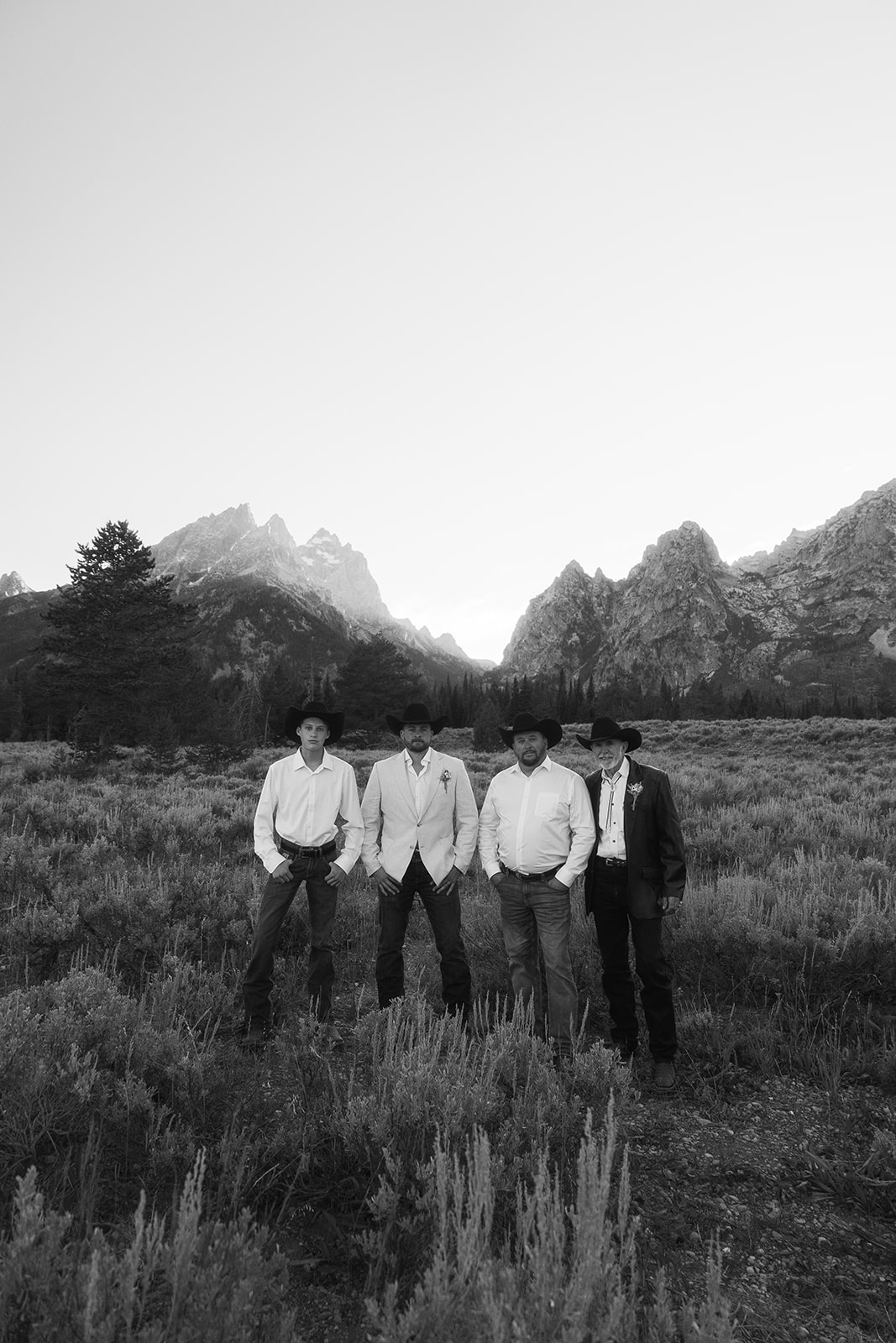 Four men in western attire stand in an open field with mountains in the background, under a clear sky at Grand Teton National park taggart lake