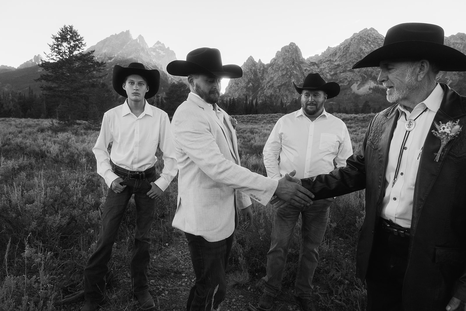 Four men in western attire stand in an open field with mountains in the background, under a clear sky at Grand Teton National park taggart lake