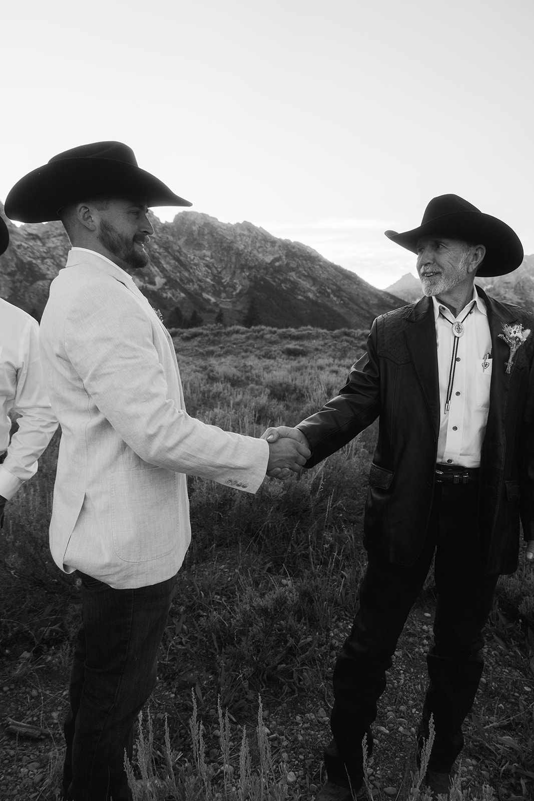 Four men in western attire stand in an open field with mountains in the background, under a clear sky at Grand Teton National park taggart lake