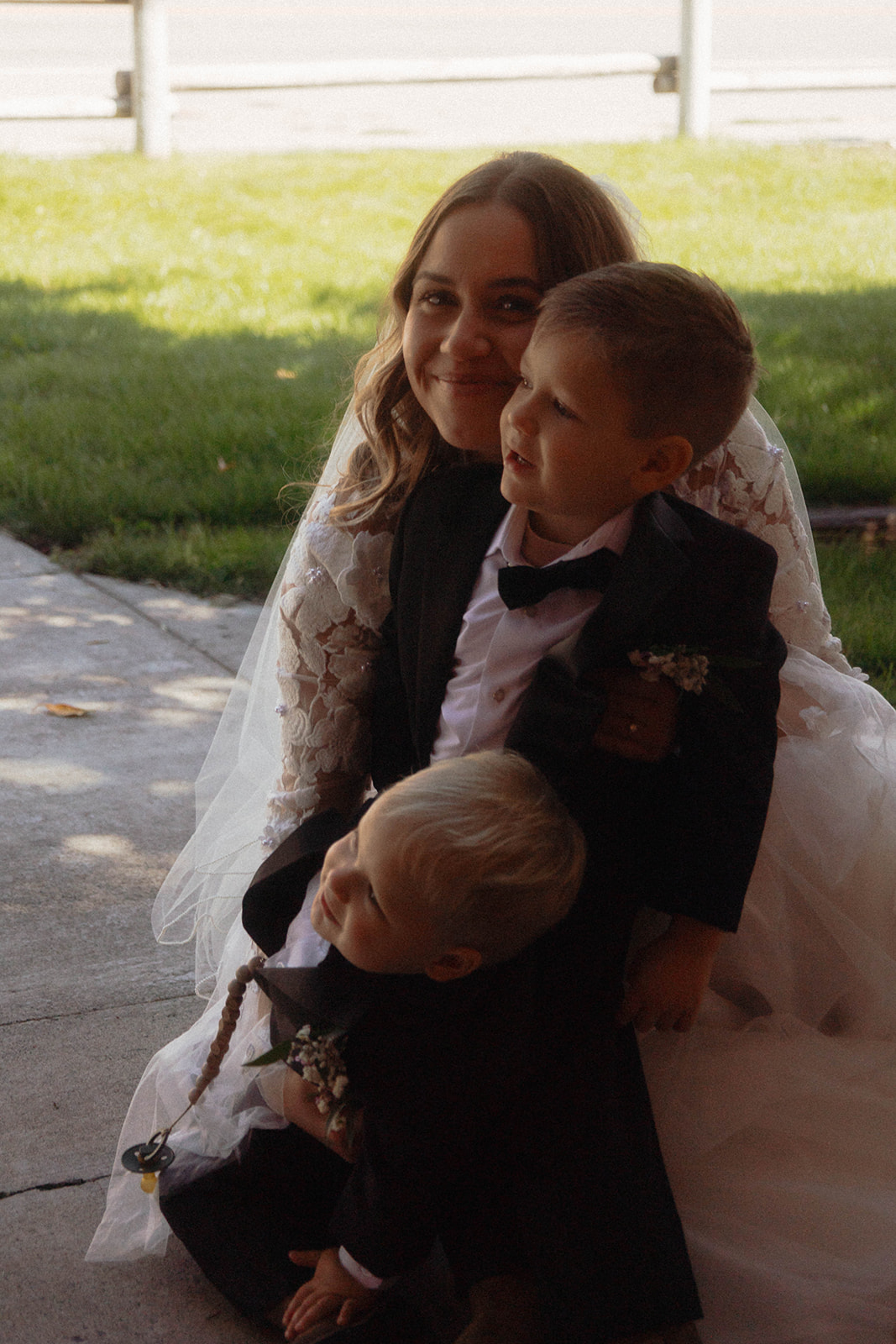 A child stands under a bride's veil, partially obscured by it. Another person is visible in the background outside. | children at your wedding