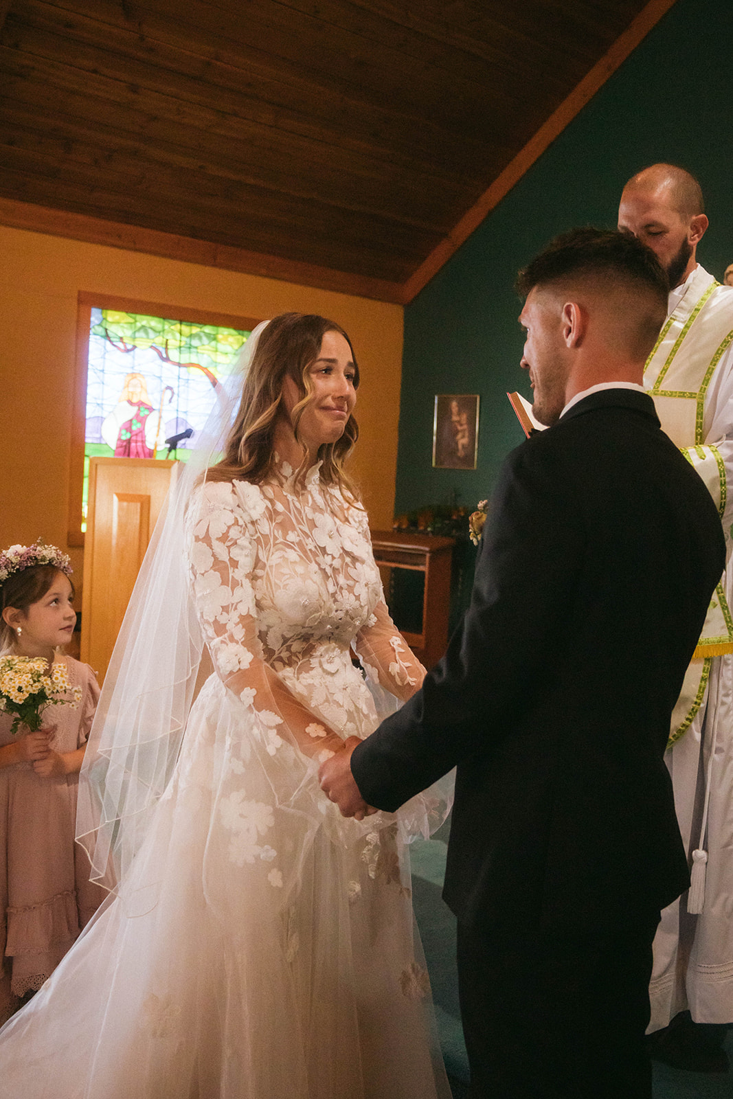 A bride and groom face each other in front of a priest during a ceremony in a church in Gardiner, Montana 