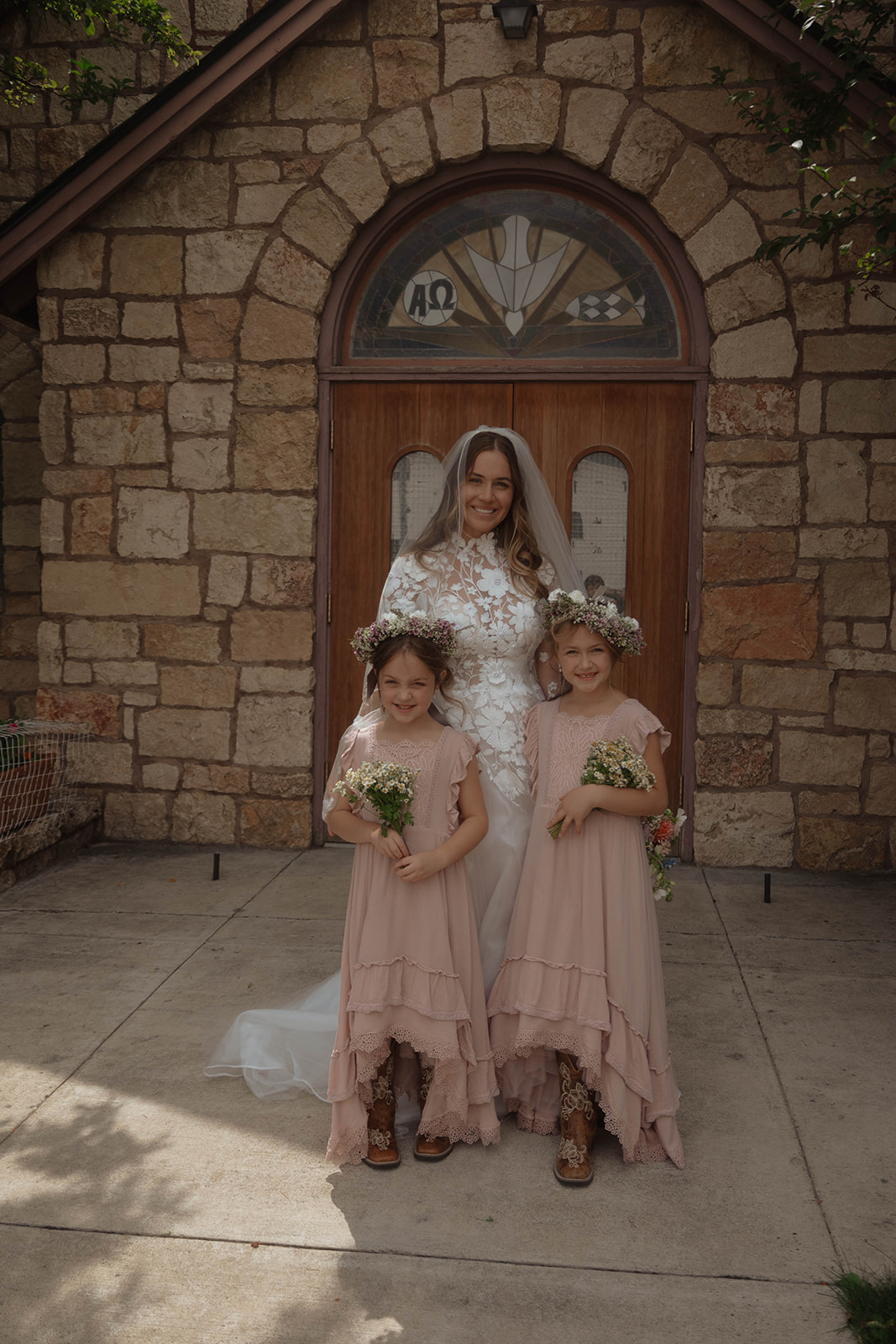 A group photo in front of a stone building shows a bride and groom with four children, two girls in pink dresses, and two boys in black suits. The bride is holding one child, and the groom holds another.